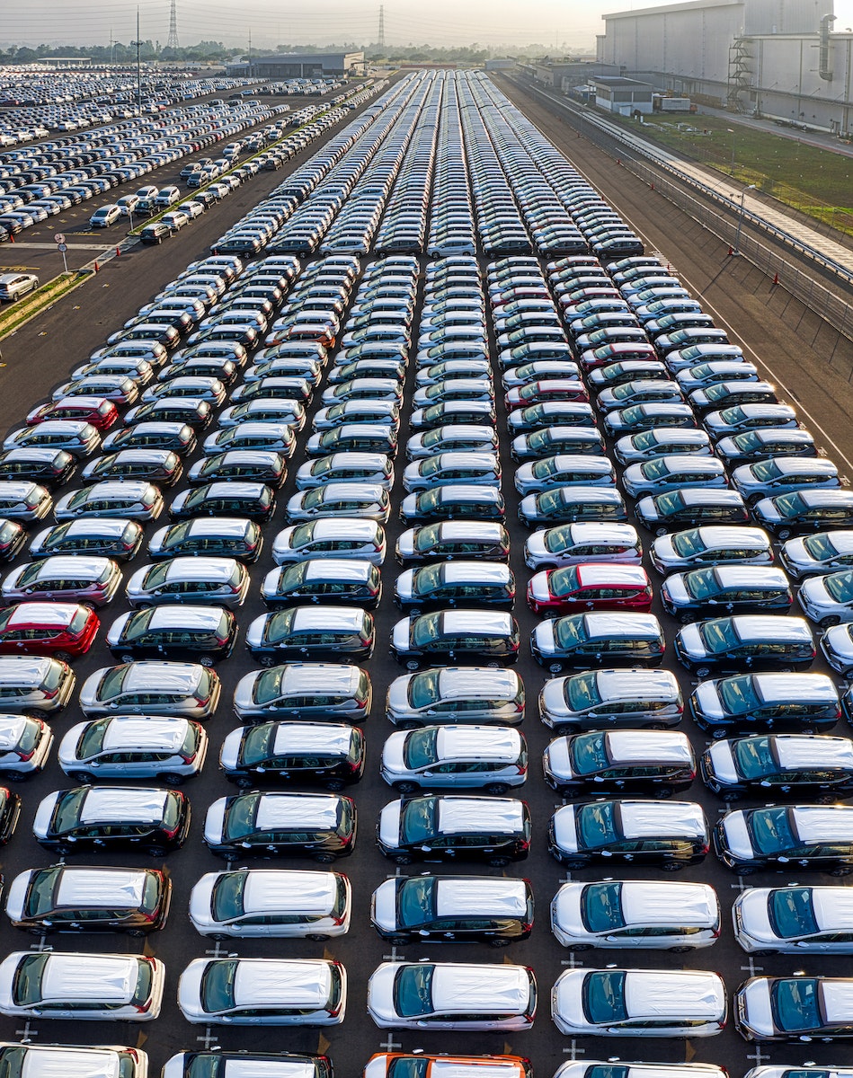 From above of many modern new automobiles placed on asphalt near factory in daytime